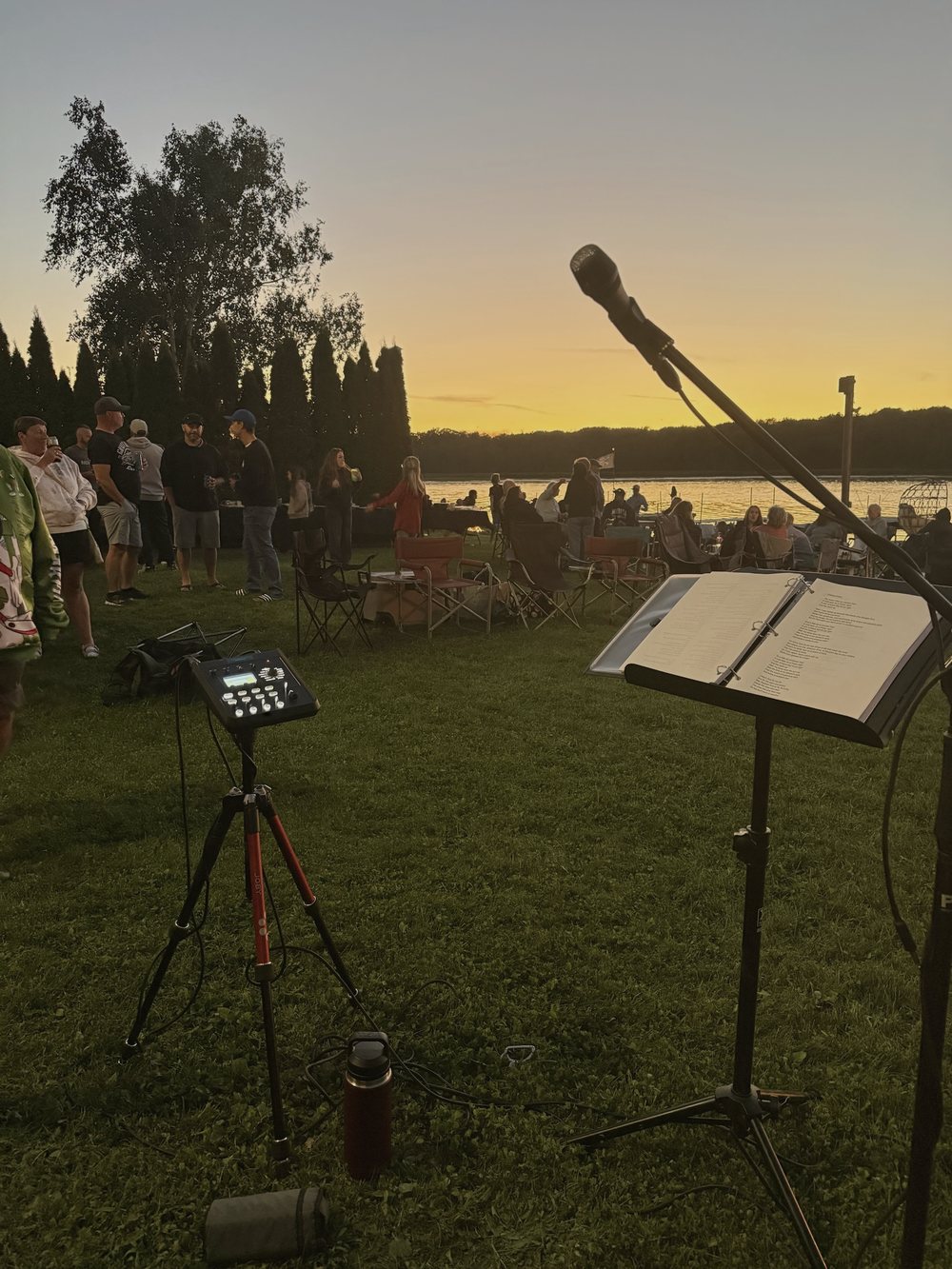 Guests on a lakeside lawn at sunset, seen from the microphone